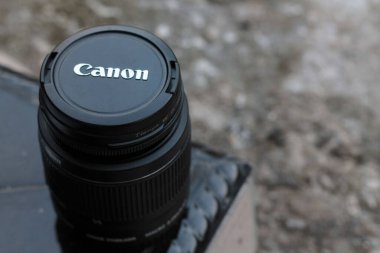 A black canon kit lens on a table on a blurry background
