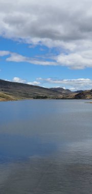 Güneşli bir baharda sakin göl üzerinde bulutlu mavi gökyüzünün dikey görüntüsü.