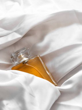 Beyaz bir kumaş arasında lüks bir kadın parfümü şişesinin dikey çekimi.