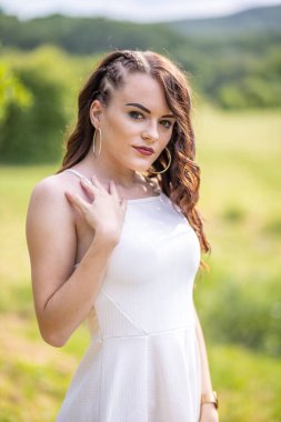 Açık havada poz veren beyaz yazlık elbiseli güzel kızın dikey yakın çekimi..