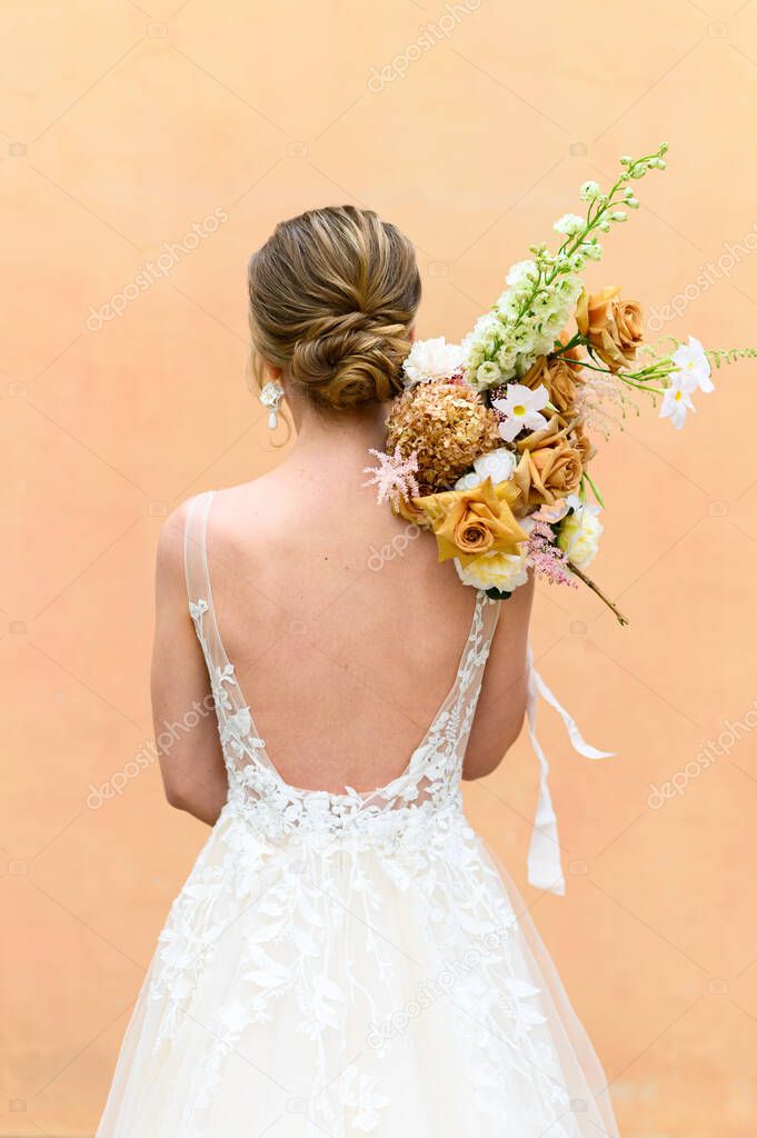 A Bride from her back in a wedding glow holding a flower bouquet over her shoulder