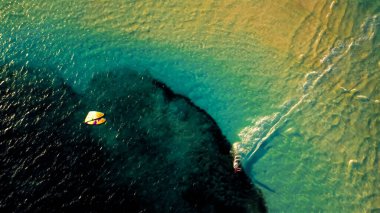 Okyanusun sığ turkuaz suyunun ve bir uçurtma sörfçüsünün hava aracı görüntüsü.
