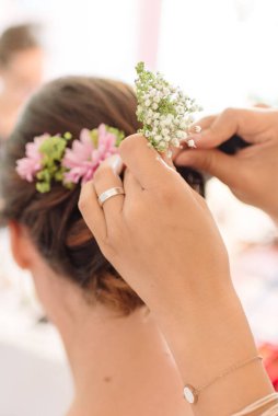 Gelinin saçına çiçek ekleyen bir stilistin dikey yakın çekimi.