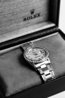 A vertical closeup of a Rolex wristwatch in a box shot in grayscale