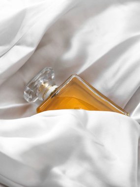 Beyaz bir kumaş arasında lüks bir kadın parfümü şişesinin dikey çekimi.