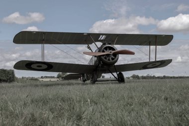 Bulutlu gökyüzünün altındaki büyük bir tarlada çimlerin üzerine park etmiş bir uçağın güzel alçak açılı görüntüsü.