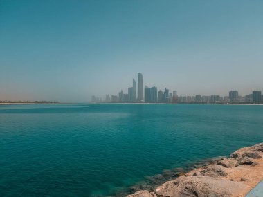 A scenic view of the blue seascape against skyscrapers on the beach on a sunny day in Abu Dhabi