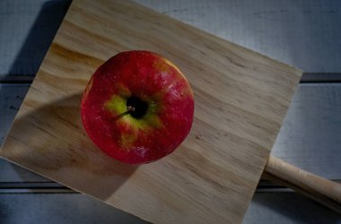 A top view of a red ripe apple with water droplets on a cutting board