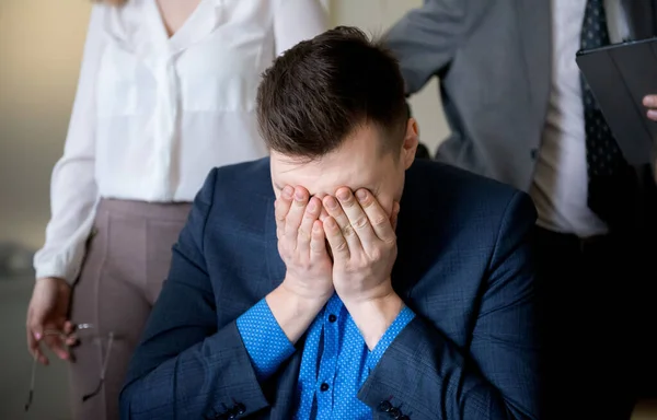 Business man covering his face with his hands, stressful situation in the workplace