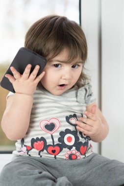 Telefonla arama yapmaya çalışan, telefonu gösteren ve onunla oynayan sevimli küçük bir kızın yakın çekimi.