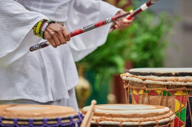 Güneşli bir günde elinde but tutan ve parkta çalan Afrikalı bir baterist.
