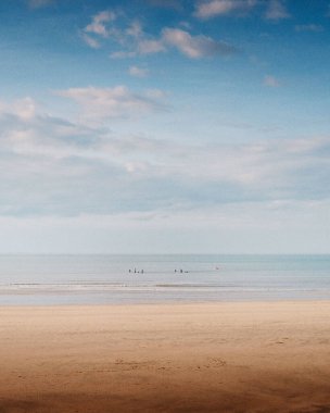 Mavi gökyüzünün altında sakin, güneşli bir sahilin dikey çekimi.