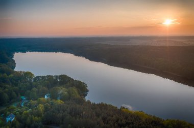 Rozalinowo Gölü 'nün insansız hava aracı görüntüsü bulutlu gökyüzünün altında gün batımıyla çevrili yeşil bir manzarayla çevrili.