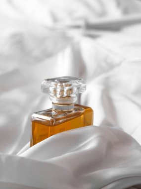 Beyaz bir kumaş arasında lüks bir kadın parfümü şişesinin dikey çekimi.