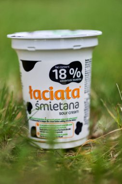 Polonyalı bir Laciata marka ekşi kremanın dikey yakın çekimi. Çimlerin üzerinde% 18 yağ var.