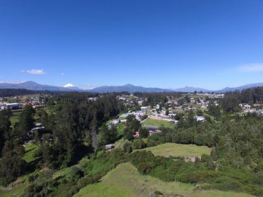 Güneşli bir günde yeşil ormanlarla kaplı tepelerin ve kırsal alandaki evlerin kuş bakışı görüntüsü
