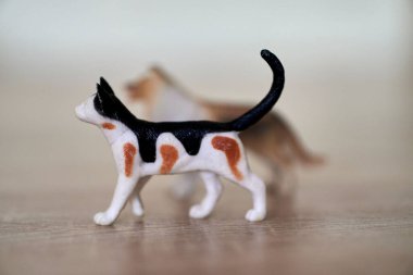 Tahta bir yüzeyde, arka planda bulanık bir oyuncakla küçük bir kedi oyuncağının yakın plan fotoğrafı.
