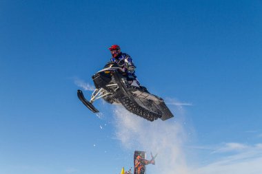 Kar arabası pistin üzerinden yükseğe zıplıyor. Kar motosikletinde, sporcuydu. Kış yarışması için bulutlu bir gün. Karda motorsporlar