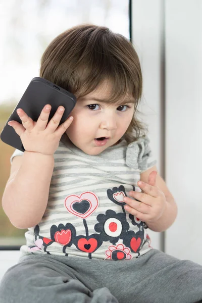 Telefonla arama yapmaya çalışan, telefonu gösteren ve onunla oynayan sevimli küçük bir kızın yakın çekimi.