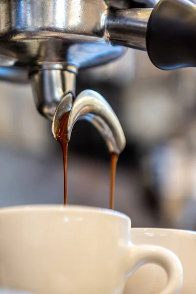A vertical closeup of the machine pouring coffee into the cups.