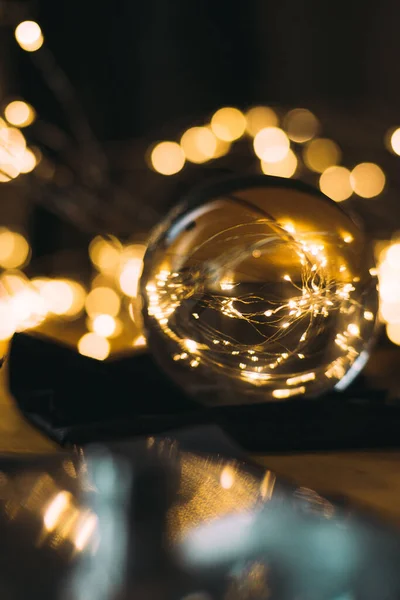 A vertical shot of fairy lights in a reflective glass ball on a bokeh background