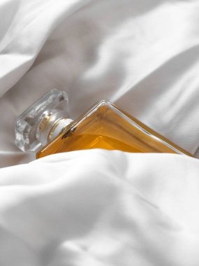 Beyaz bir kumaş arasında lüks bir kadın parfümü şişesinin dikey çekimi.