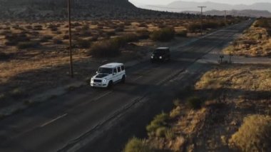 A drone shot of black and white Mercedes-Benz G-class cars driving in the Palmdale desert