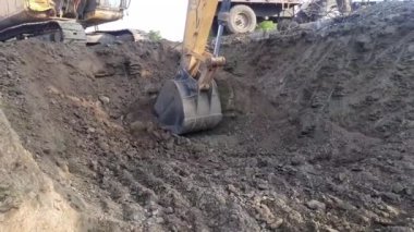 A JCB excavator machine loads Moorum soil into a tractor at construction land. Labor breaking rocks for construction work. JCB machine work in progres