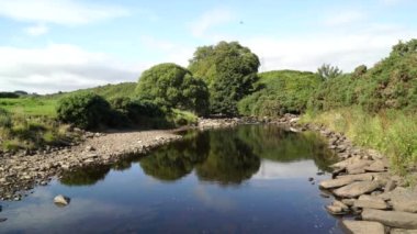 A scenic view of a slow flowing river surrounded by greenery in Dunbeath Strath, Scottish Highlands
