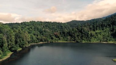 A drone shot over a beautiful lake surrounded with green trees under cloudy sky