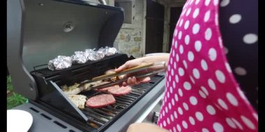 A closeup shot of a female in an apron flipping patties on a grill