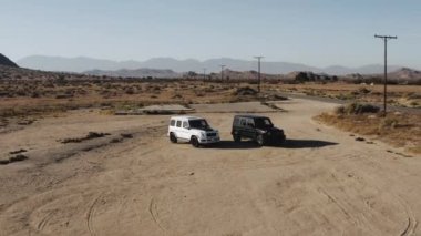 A drone shot of black and white Mercedes G Wagon cars parked in the middle of desert area
