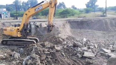 An excavator bucket collects clay stone moorum (murum) from the pit and pours it onto a large pile of clay rock.