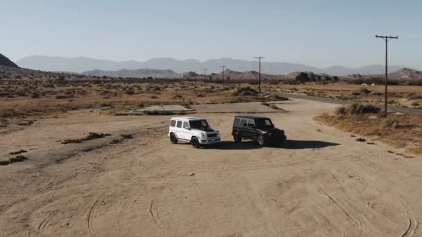 砂漠の真ん中に停まっている黒と白のメルセデスGワゴン車のドローンショット — ストック動画