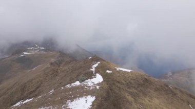 A top view of a hiker on the top of snow covered mountain under foggy clouds