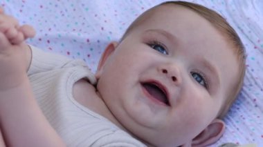 A closeup shot of an adorable blonde blue-eyed baby laughing and playing