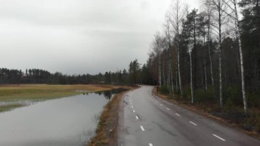Two cyclists riding on a small road passing through a mossy lake and a forest in Falun, Sweden