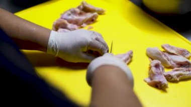 A closeup shot of a man's hands cutting a piece of chicken into pieces with a sharp knife