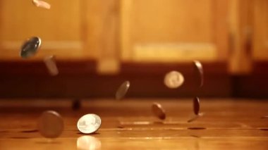 A bunch of silver and bronze coins falling and rolling around on a wooden floor