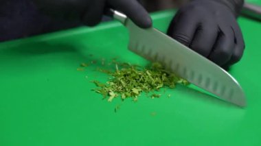 A closeup shot of a person in black gloves cutting parsley on a green cutting board