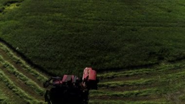 Aerieal drone of norwegian farmer driving tractor cutting green pasture grass while driving in a nice pattern to be collected for livestock