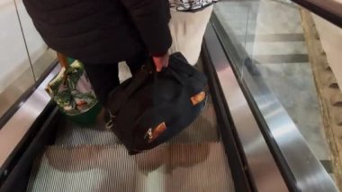 Man holding a bag down the electric escalator indoors