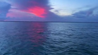 An aerial shot of blue sea waves with a red bright sunset reflected on them