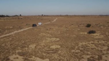 A black car and white car driving down a narrow road in the desert
