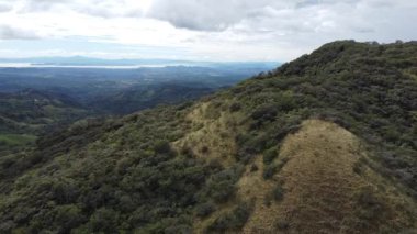 The aerial drone footage of the green hills against the background of the cloudy sky.