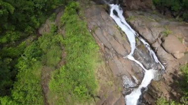 An aerial view of a beautiful mountain waterfall with green plants and trees growing around on a sunny day