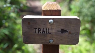 A closeup footage of a wooden Trail sign over a blurry background of a field