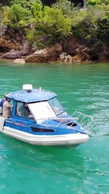 The vertical drone footage of the boat taking a tour on a turquoise calm and clean ocean water  around the mountainous land, New Zealand