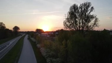 The busy roads in the suburbs with dense forest on the left during a scenic sunset in Radom