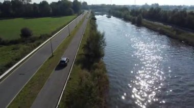 A beautiful view of a car driving on a road with a river on the other side